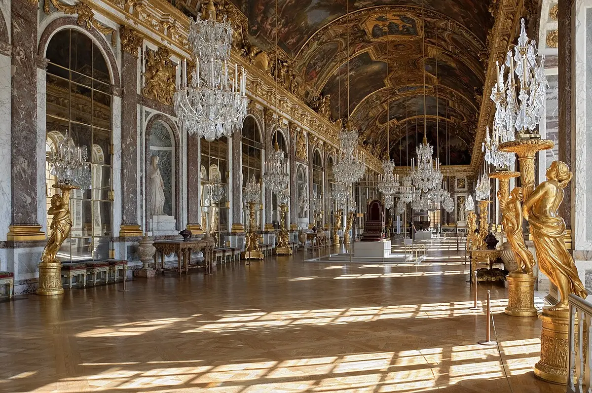 The Hall of Mirrors at Versailles, chandeliers and gilded statues along a mirrored wall facing tall windows