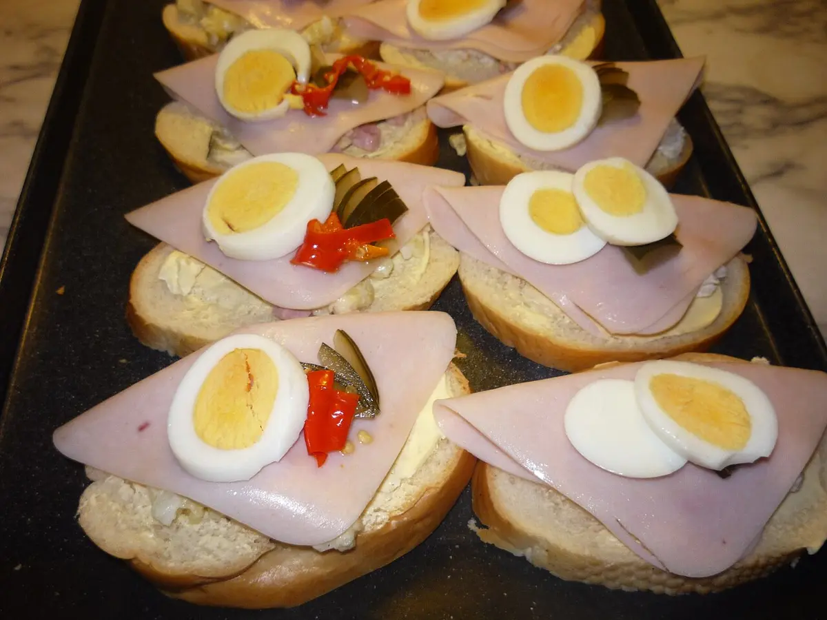 A tray of chlebíčky, open sandwiches with ham, egg, pickles and red pepper