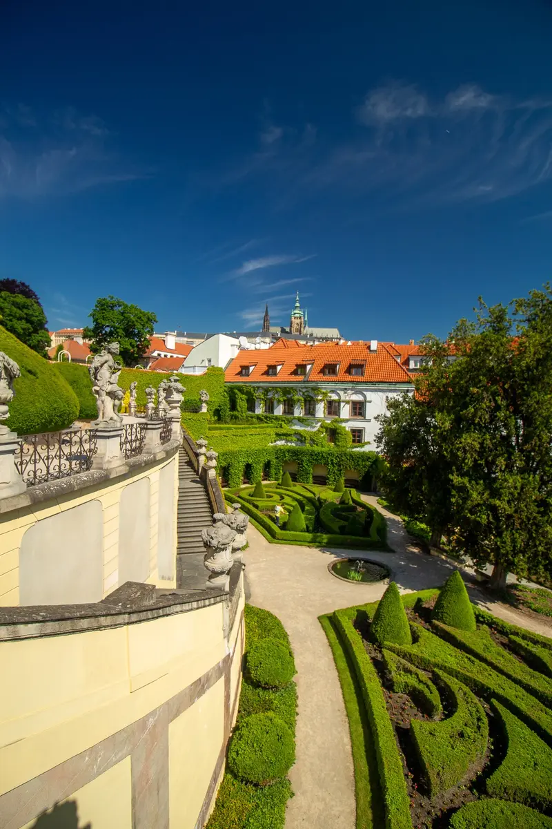 The terraced Vrtba Garden with baroque statues and clipped hedges, St. Vitus Cathedral above the roofs