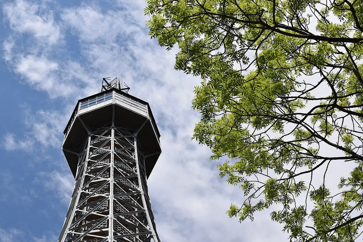 The steel lattice top of the Petřín Lookout Tower against the sky, framed by leaves