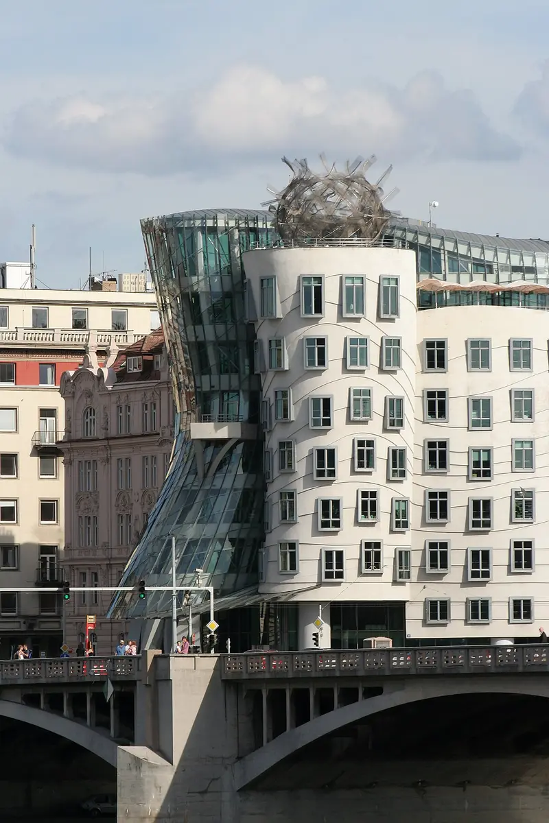 The Dancing House: a leaning glass tower beside a curving white tower with a metal crown, seen across the bridge