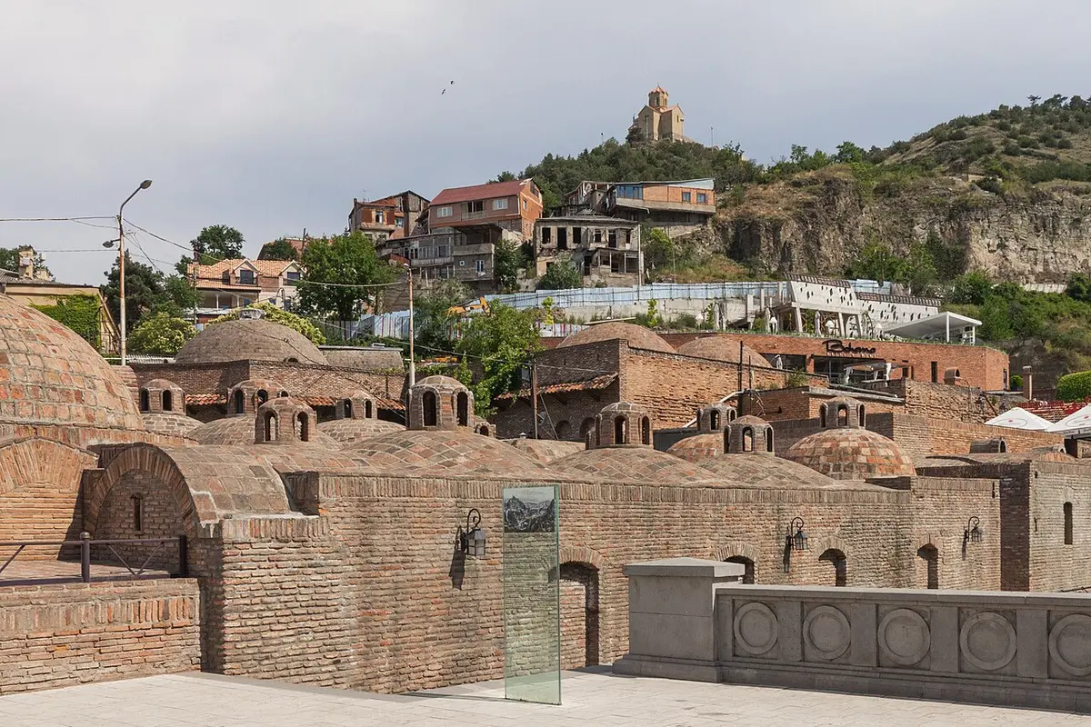 The low brick domes of the sulphur bathhouses in Abanotubani, with old houses and a hilltop church behind