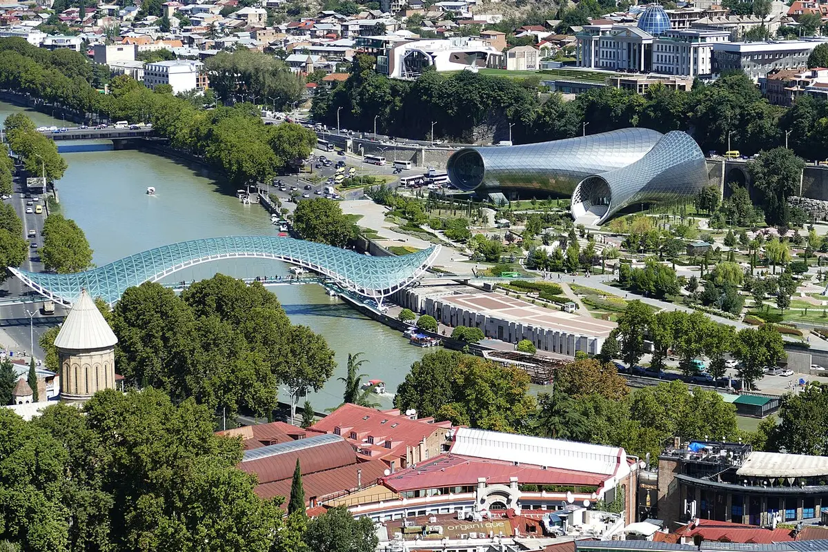 The curving glass canopy of the Bridge of Peace over the Mtkvari, with Rike Park and two silver tube-shaped buildings beyond