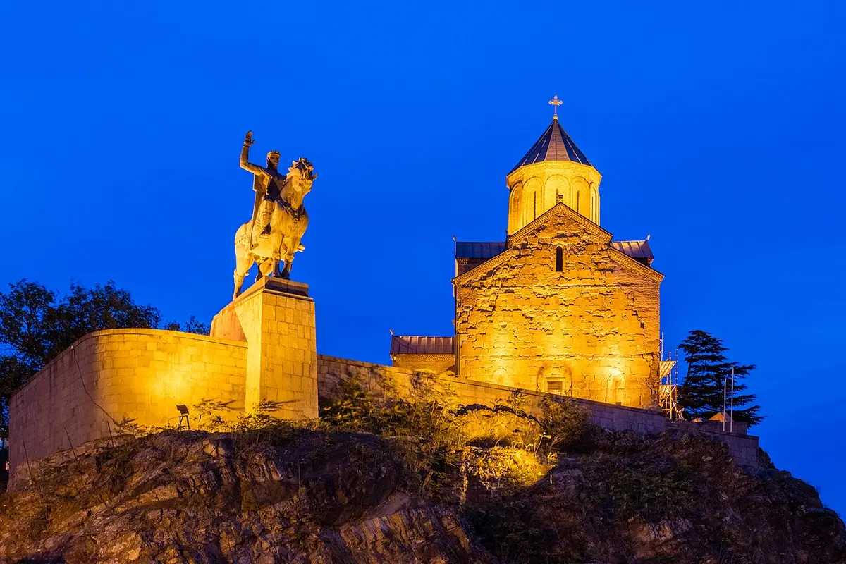 Metekhi Church and the bronze equestrian statue of Vakhtang Gorgasali, lit up at dusk on the cliff above the river
