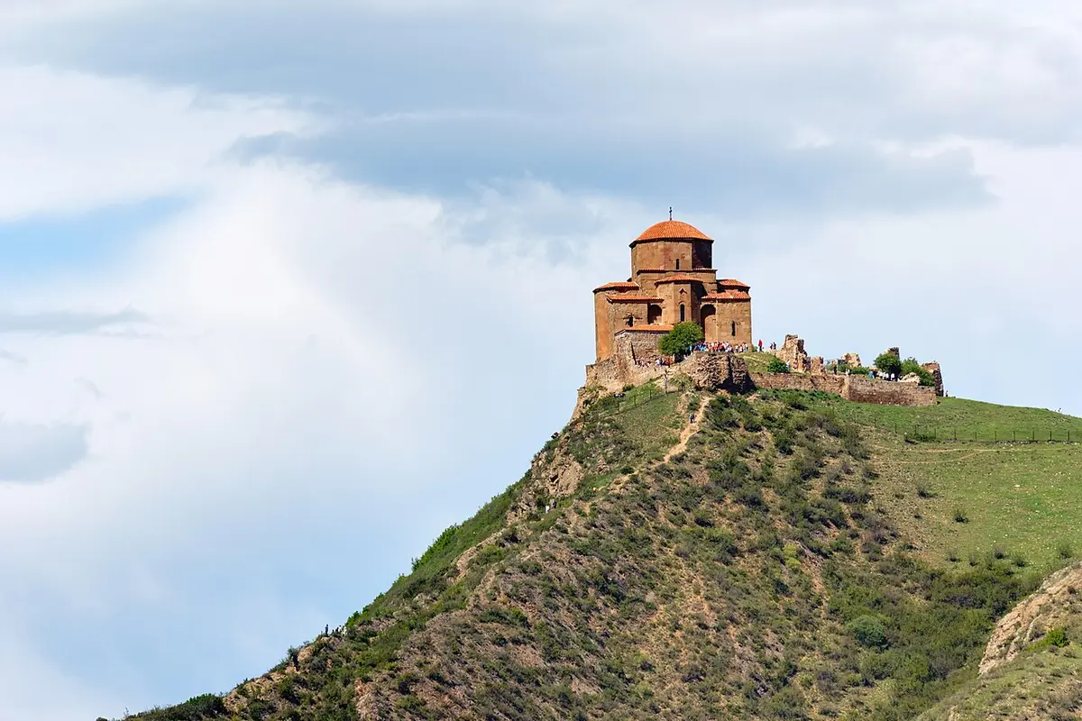 Jvari Monastery, a small domed stone church, on top of a steep green hill