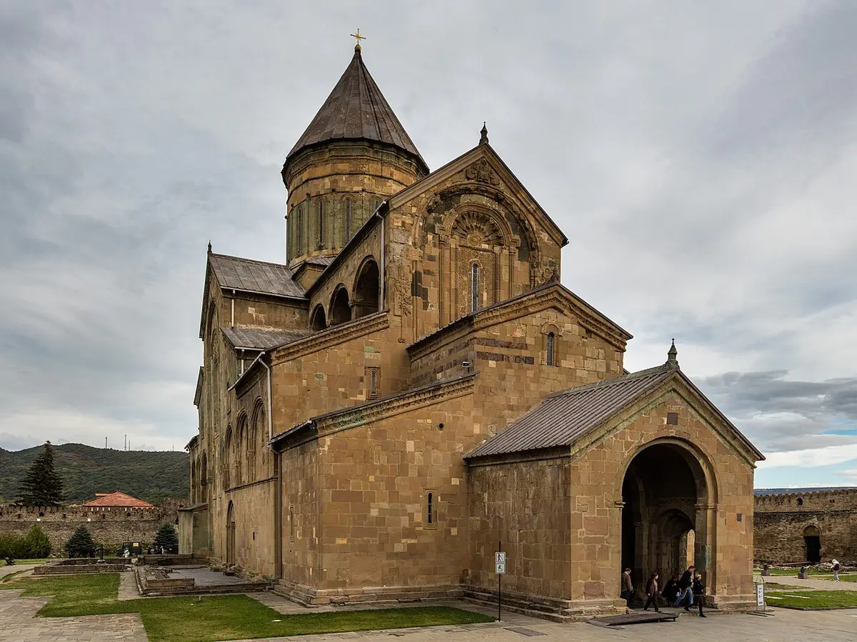 Svetitskhoveli Cathedral, a large stone church with a conical dome, seen from its walled courtyard