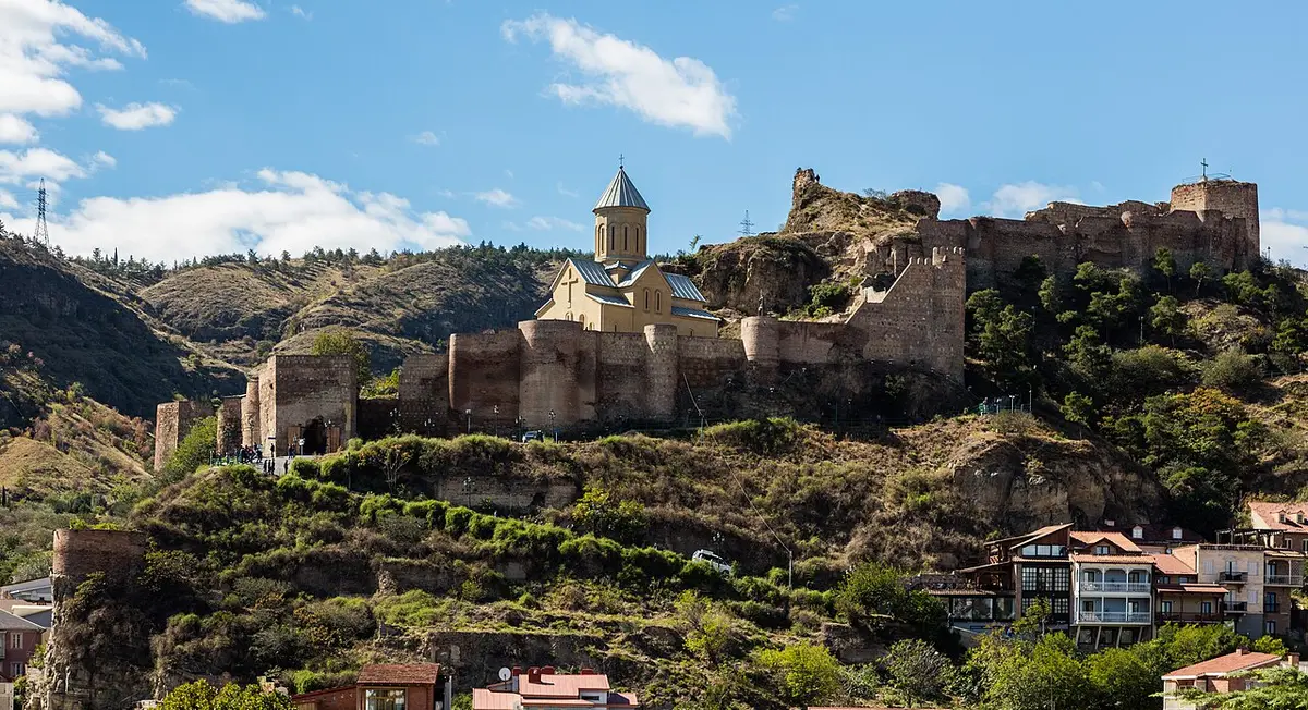 The stone walls of Narikala Fortress along a rocky ridge, with the domed church of St. Nicholas inside them