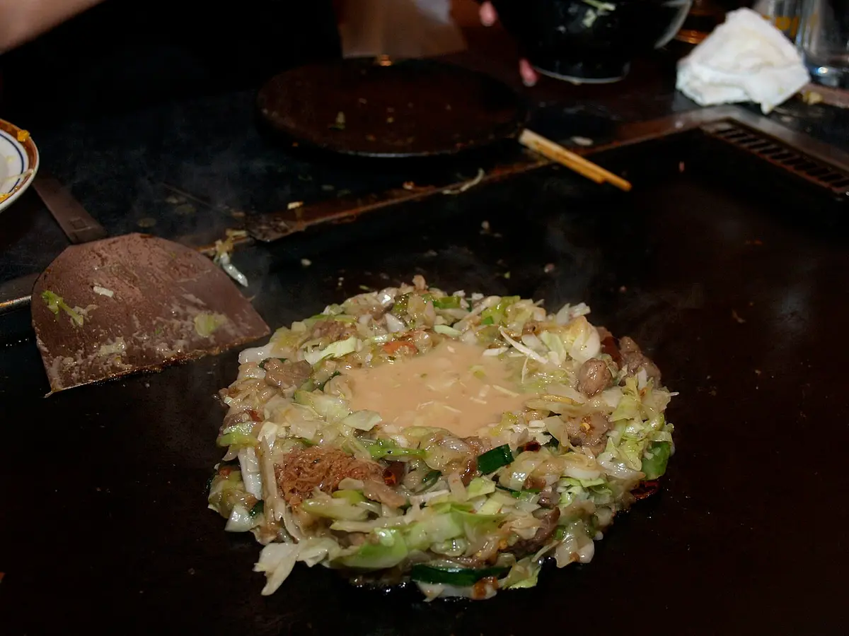 Monjayaki cooking on a griddle, a ring of chopped cabbage around a pool of batter