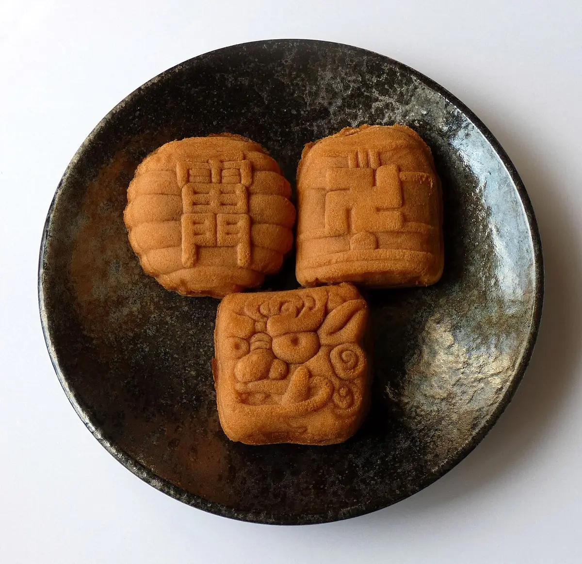 Three small ningyō-yaki cakes on a dark plate, one shaped like the Kaminarimon lantern