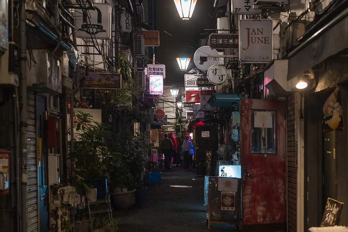 A narrow lane of tiny bars in Golden Gai at night, lit by small signs