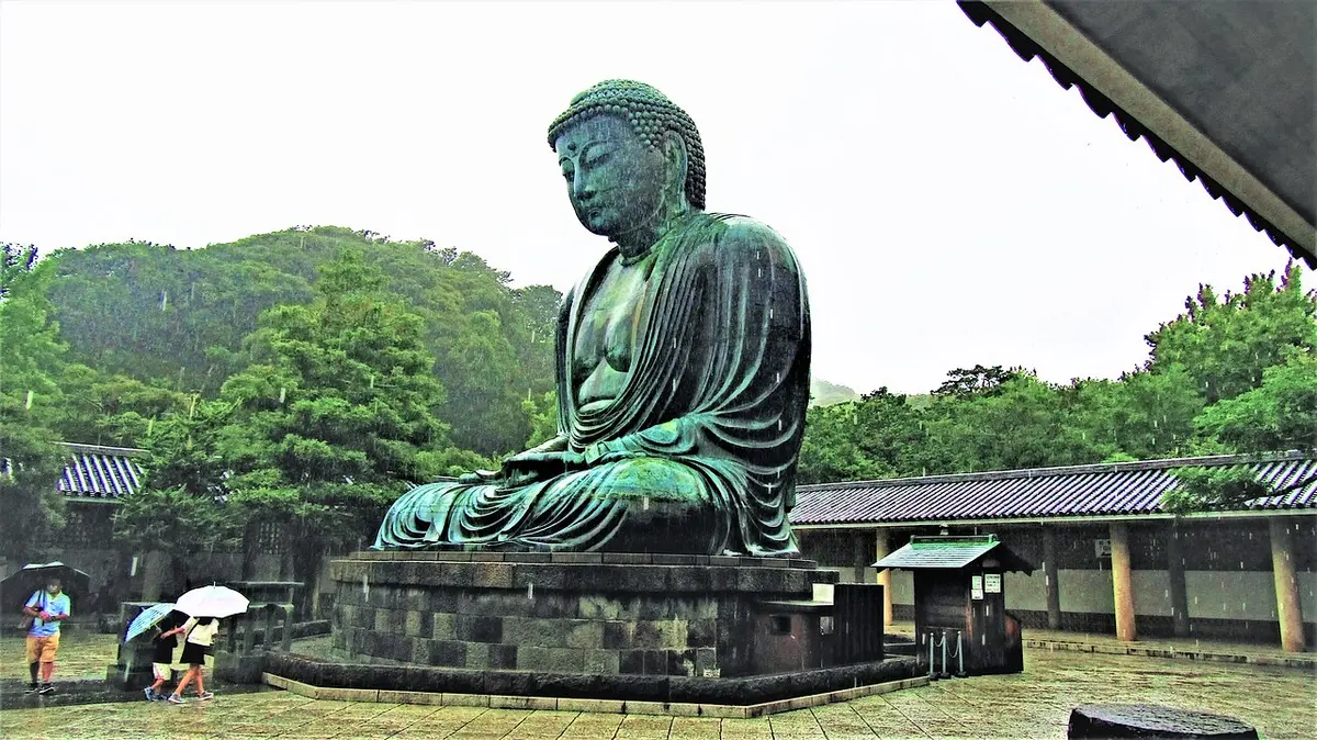The bronze Great Buddha of Kamakura seated in the open, with green hills behind