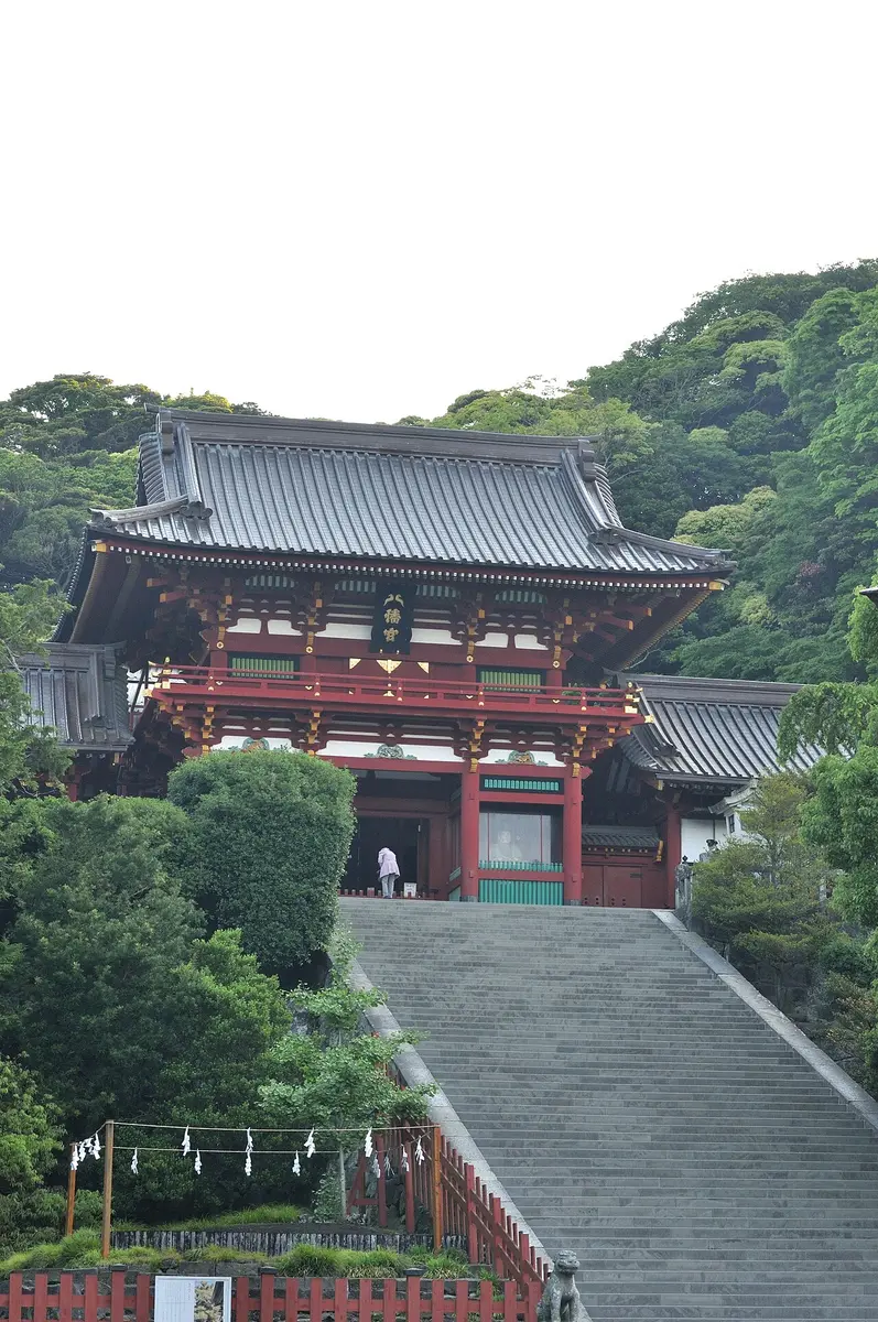 The red gate of Tsurugaoka Hachimangū’s upper shrine at the top of a long flight of stone steps, wooded hills behind