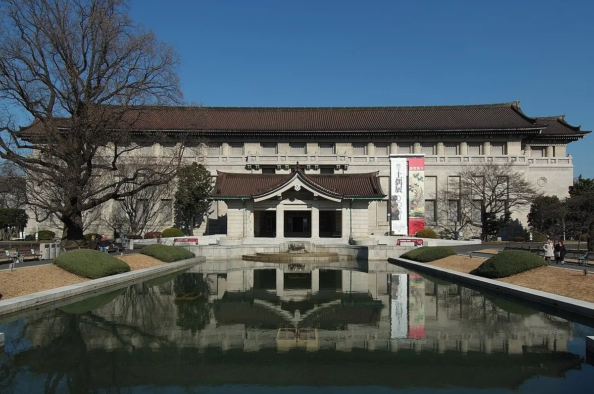 The main building of the Tokyo National Museum, with a tiled roof, reflected in a long pool