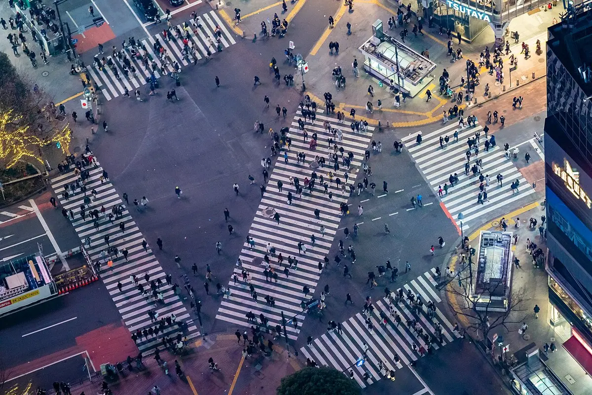Shibuya Crossing at night seen from high above, crowds walking across the diagonal stripes