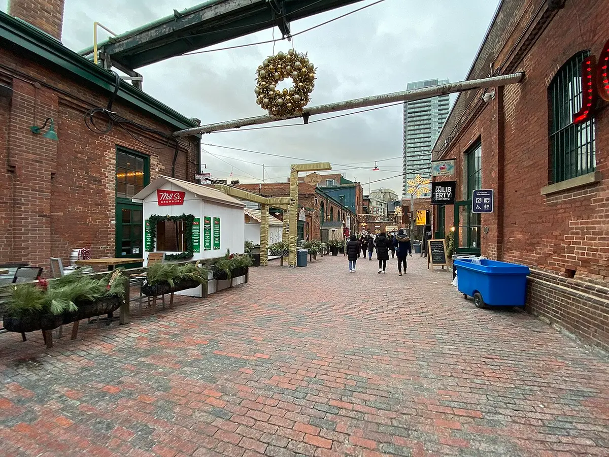 A brick-paved lane between Victorian red brick buildings in the Distillery District, a wreath hung across it