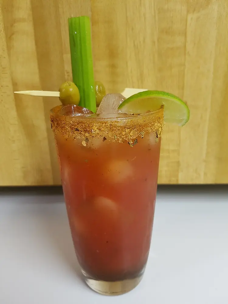 A Caesar cocktail in a spice-rimmed glass with celery, olives and a lime wedge