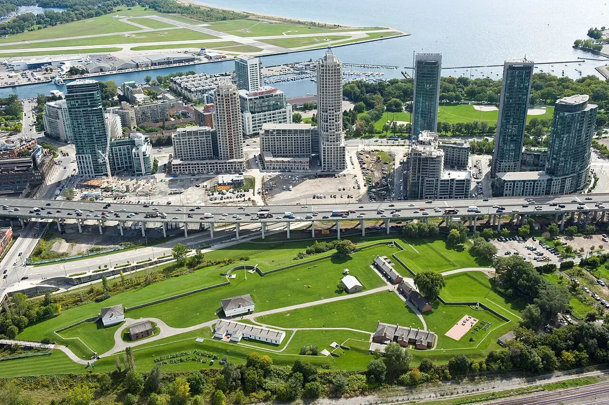 Aerial view of Fort York’s green earthworks and low buildings, the Gardiner Expressway and condo towers beyond