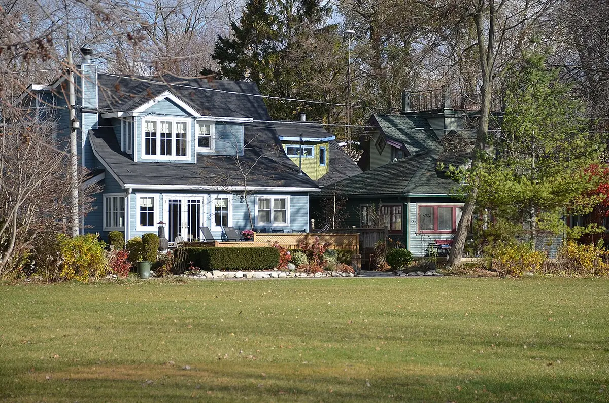 A blue clapboard cottage behind a wide lawn and trees on Ward’s Island