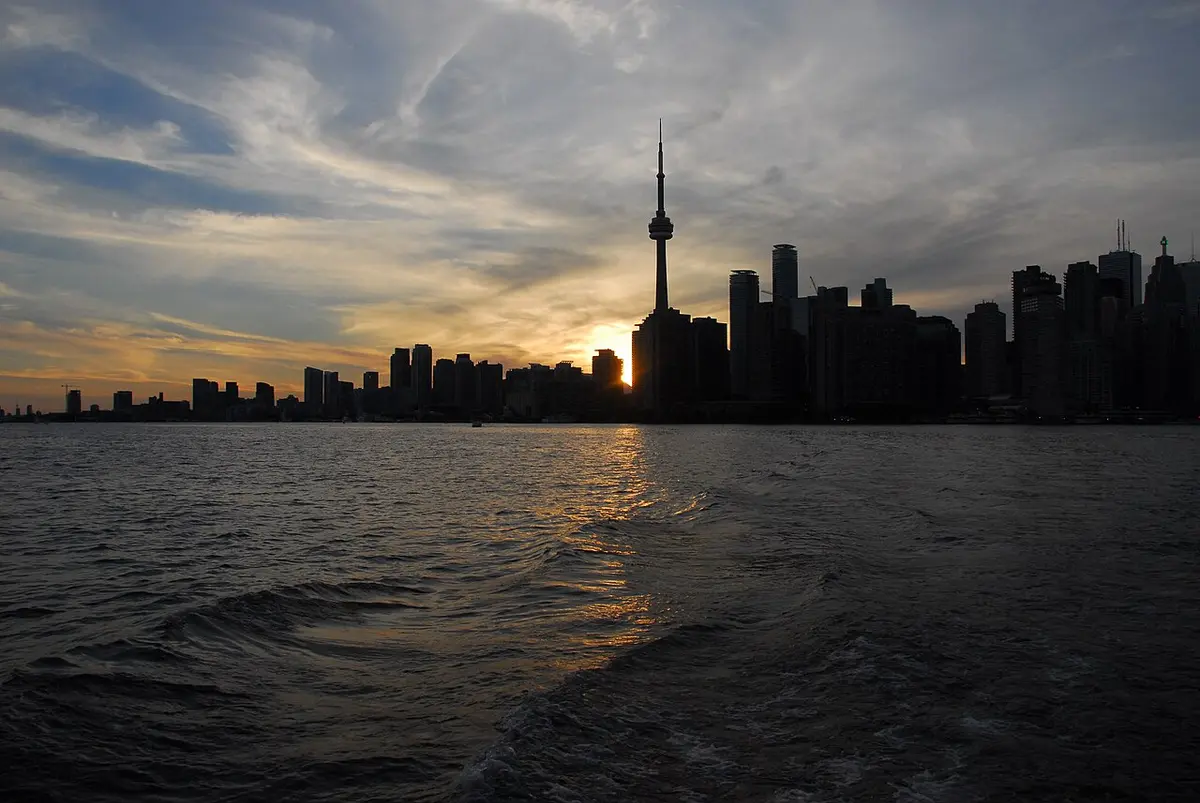 The Toronto skyline and the CN Tower in silhouette against a sunset sky, seen from a ferry