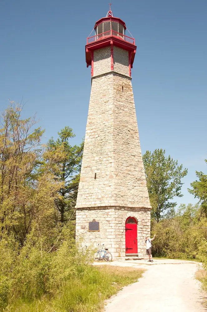 The stone tower of Gibraltar Point Lighthouse with its red lantern and door, among trees