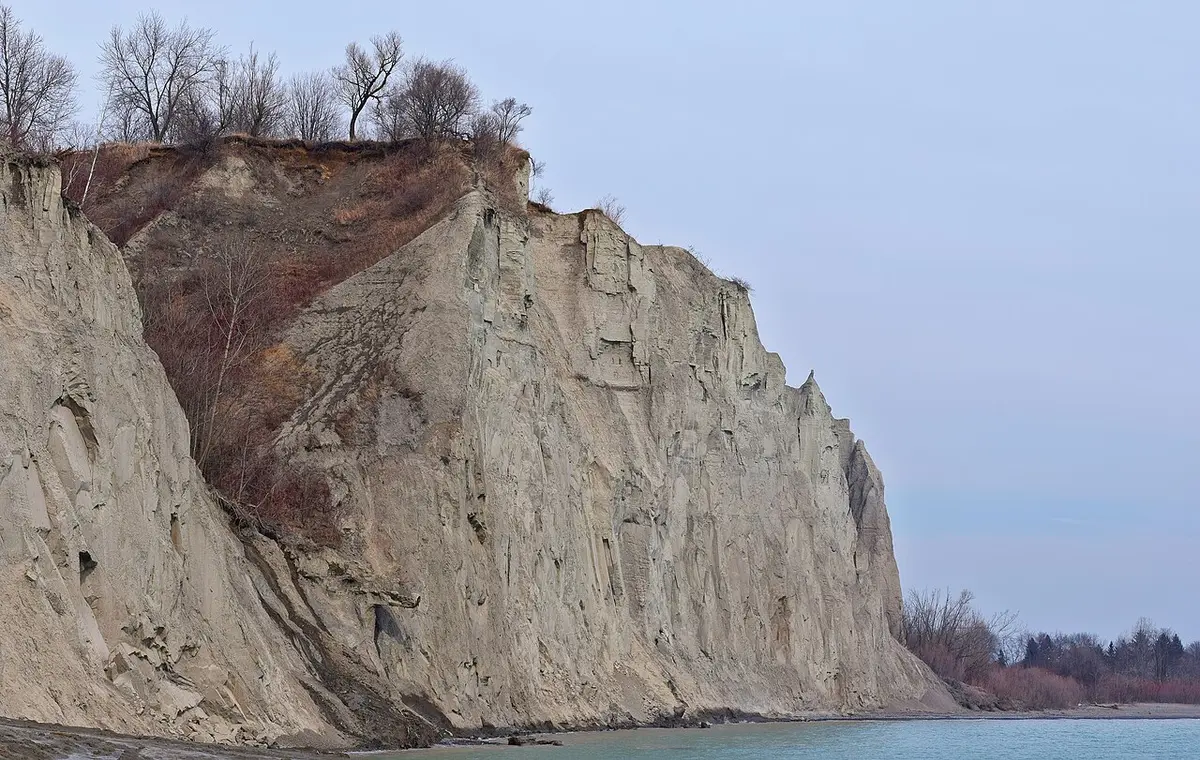 A tall pale cliff of the Scarborough Bluffs above the shore of Lake Ontario