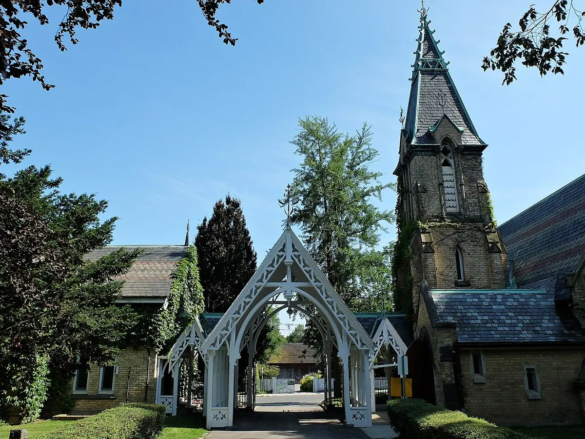 The white Gothic wooden gate of the Toronto Necropolis beside its stone chapel and spire