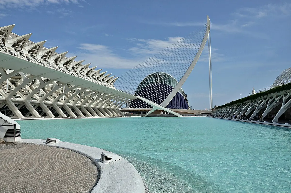 The white ribbed Science Museum beside a turquoise pool, with the blue dome of the Àgora and the white mast of the Assut de l’Or bridge behind