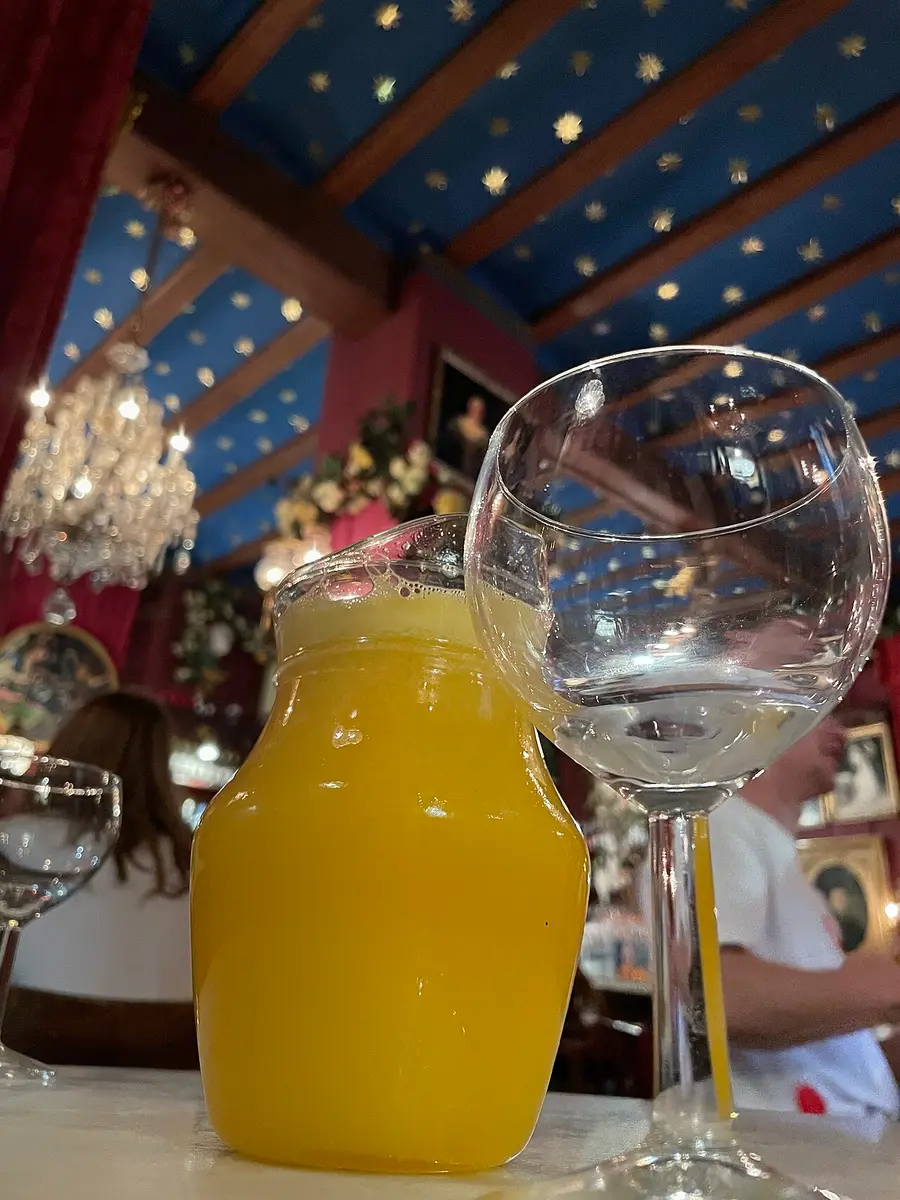 A jug of bright orange Agua de Valencia beside an empty glass on a café table