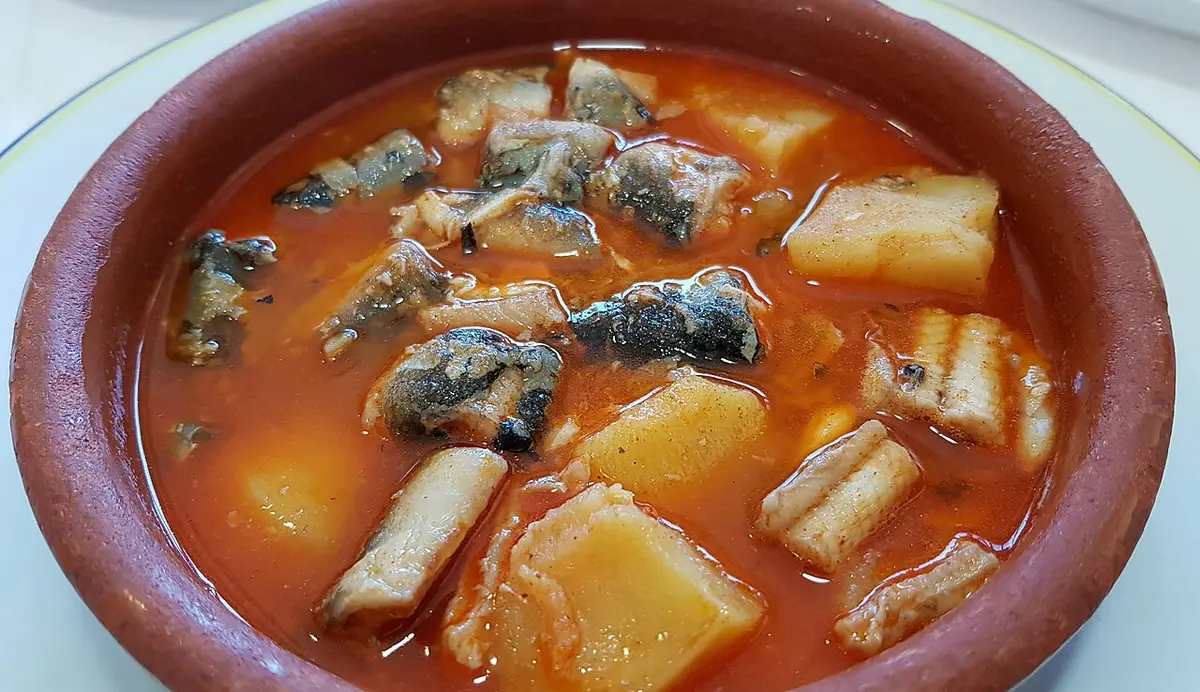 Pieces of eel and potato in a red garlic and paprika sauce in a clay dish