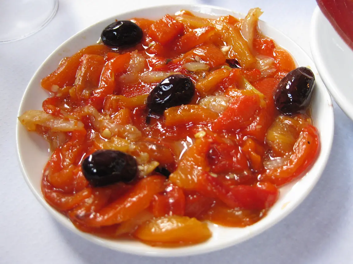 Strips of roasted red pepper and salt cod with black olives on a white plate