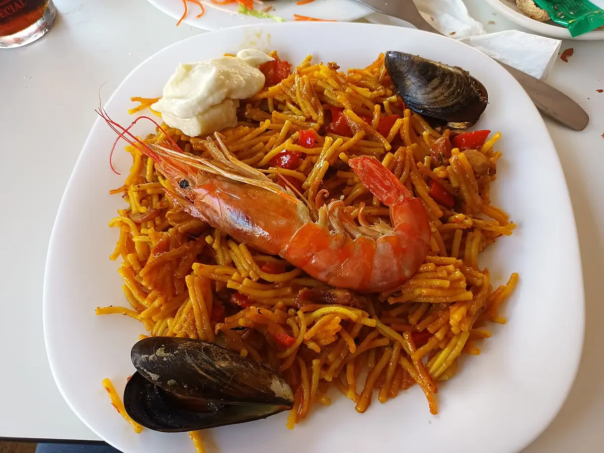 A plate of fideuà, short noodles with prawns and mussels and a spoonful of allioli