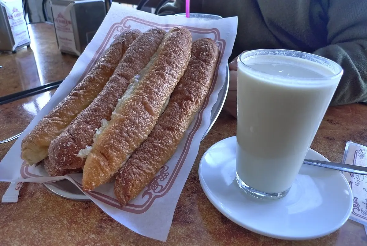 A glass of horchata beside three long glazed fartons on a paper napkin