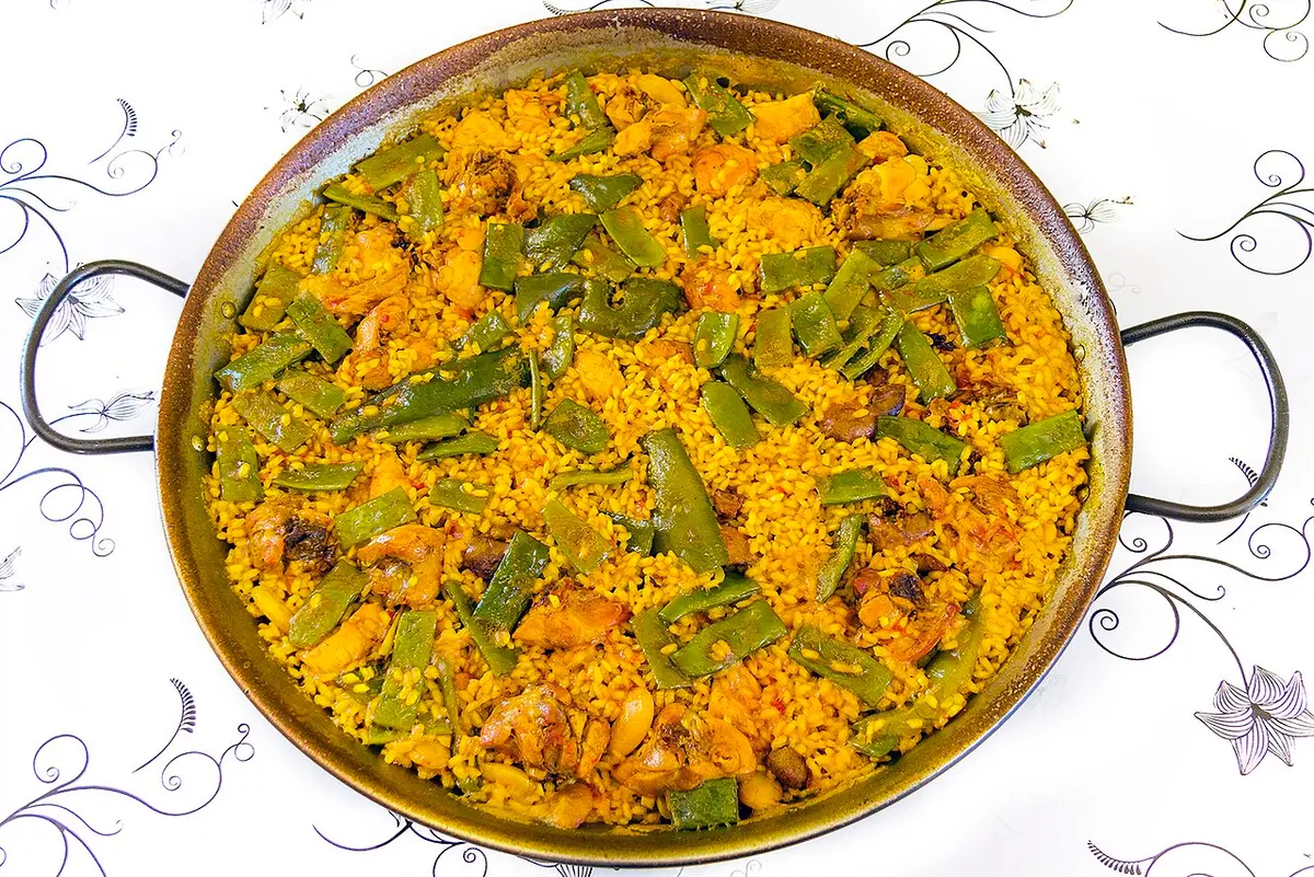 A paella valenciana in its wide pan, with chicken, rabbit, green beans and large white beans