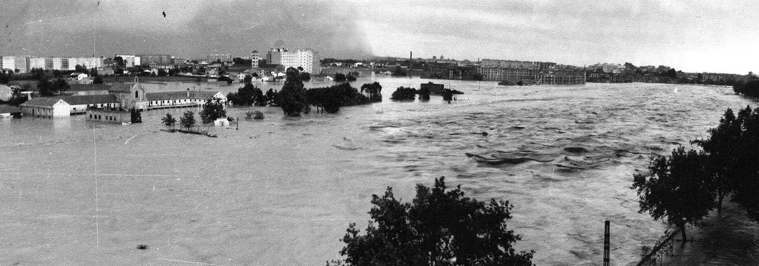 Black and white photograph of the flooded Turia spreading across the city, buildings and treetops standing out of the water