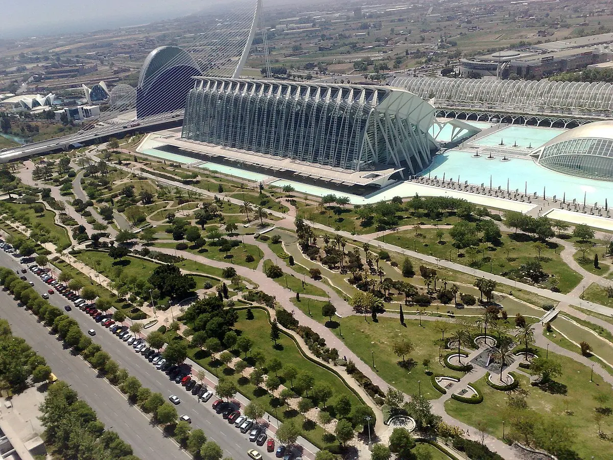 The Turia gardens from above, paths and trees filling the old riverbed beside a road, with the City of Arts and Sciences beyond