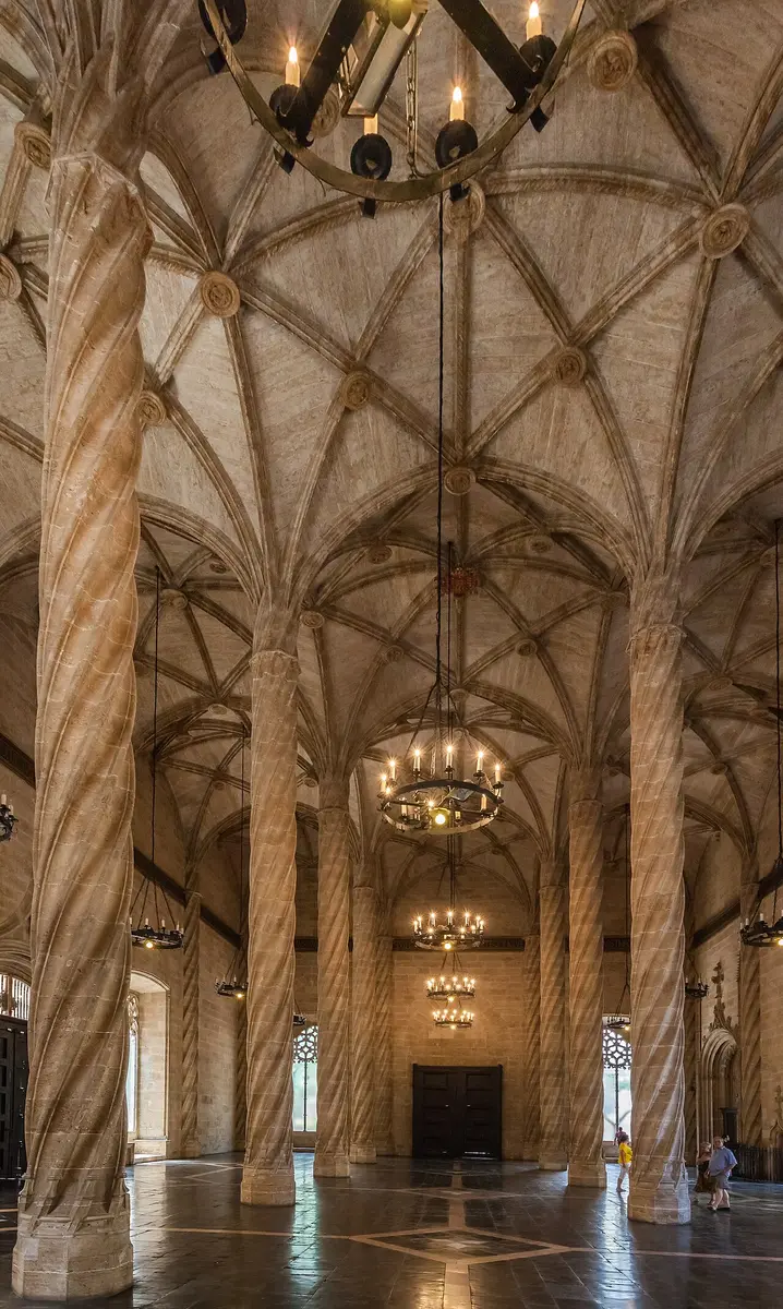 Twisted stone columns branching into a ribbed Gothic vault in the Hall of Columns of the Silk Exchange, with iron chandeliers