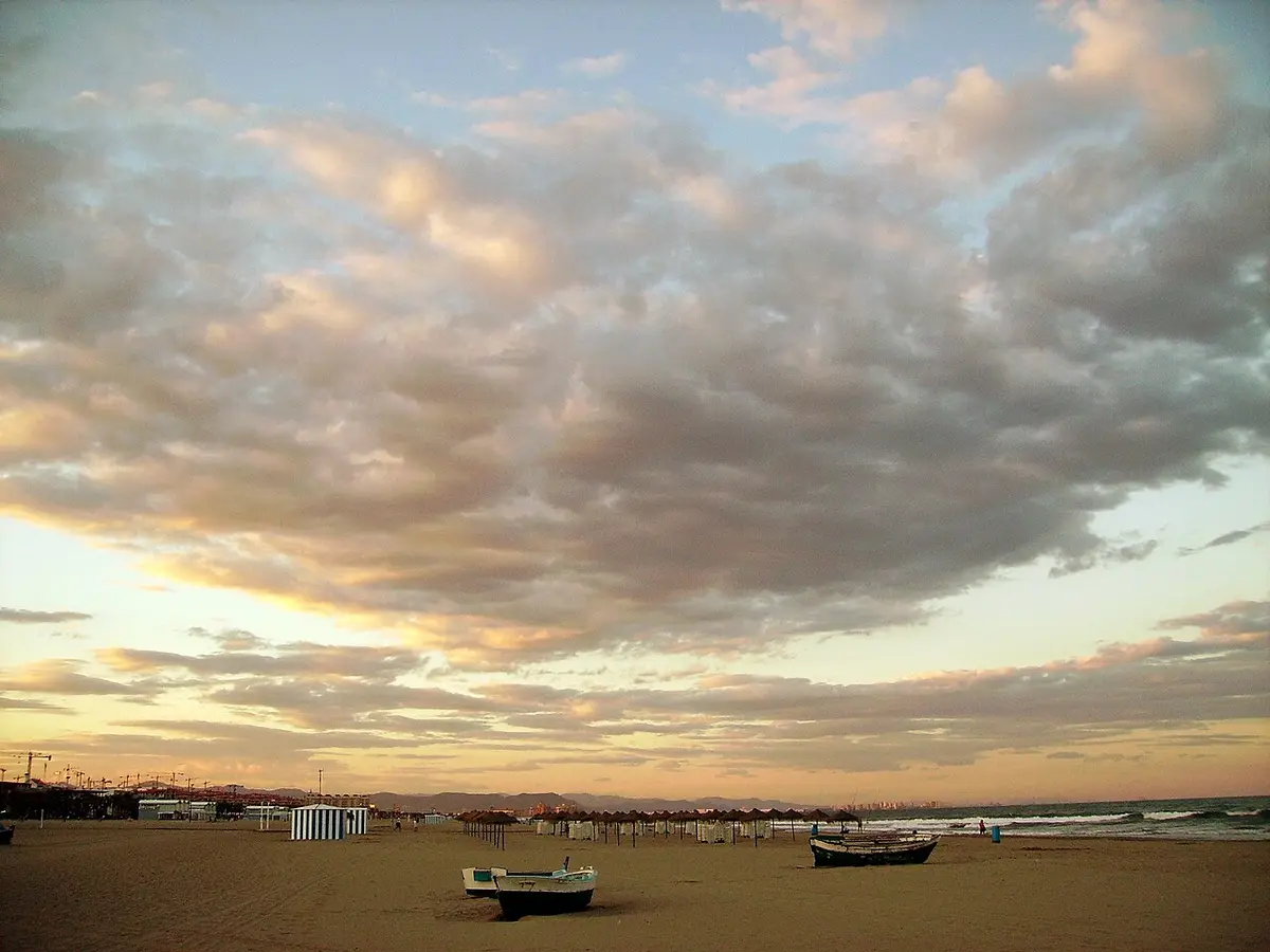 The wide sand of the Malvarrosa beach in Valencia at dusk, a few boats drawn up on the beach