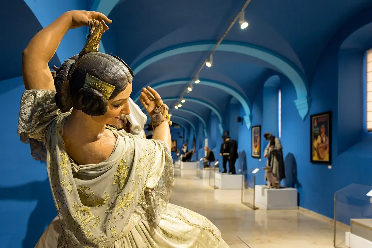 A pardoned ninot of a woman in traditional Valencian dress, arms raised, in a blue gallery of the Fallas Museum