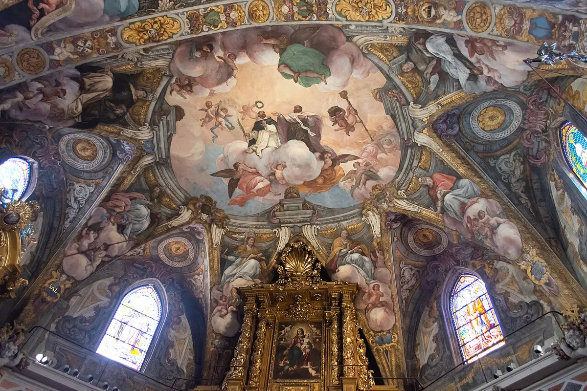 The frescoed vault of the church of San Nicolás, painted saints in glory among gilded ornament, with the top of the altarpiece below