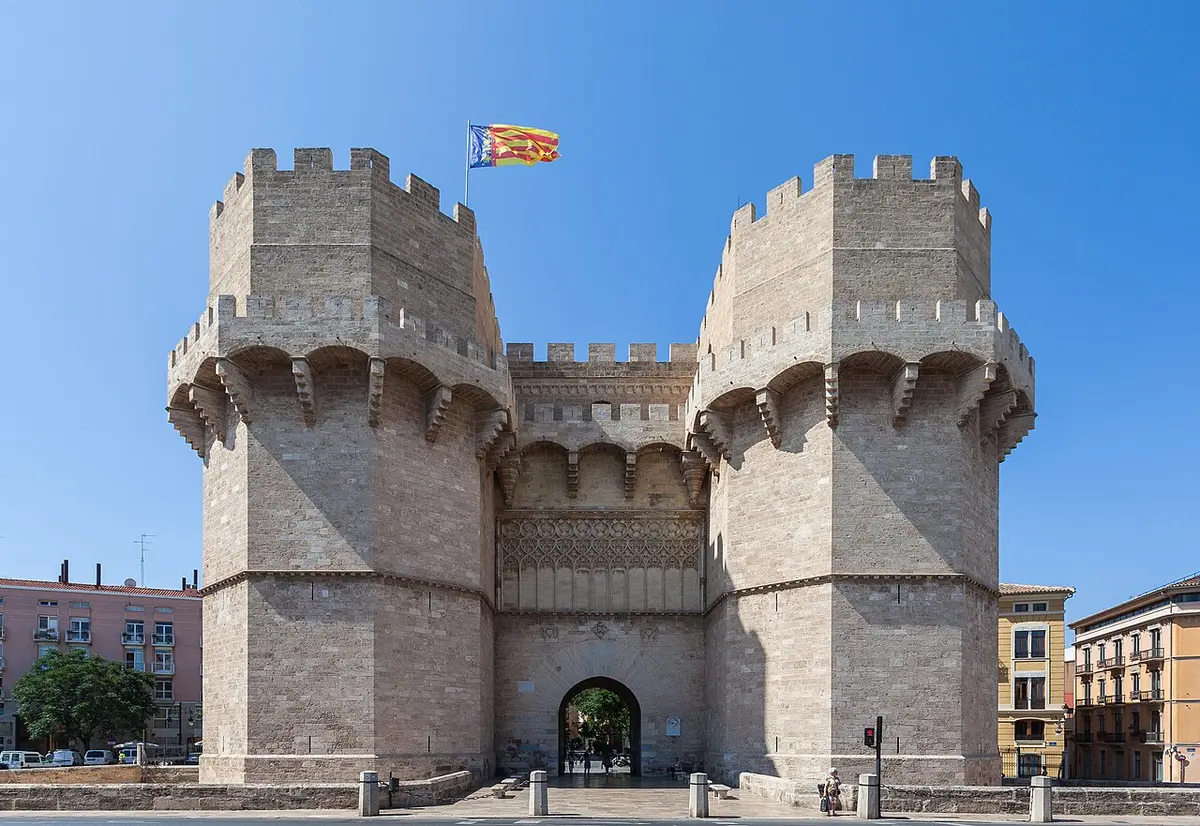The two crenellated towers of the Serranos gate under a blue sky, a flag flying above