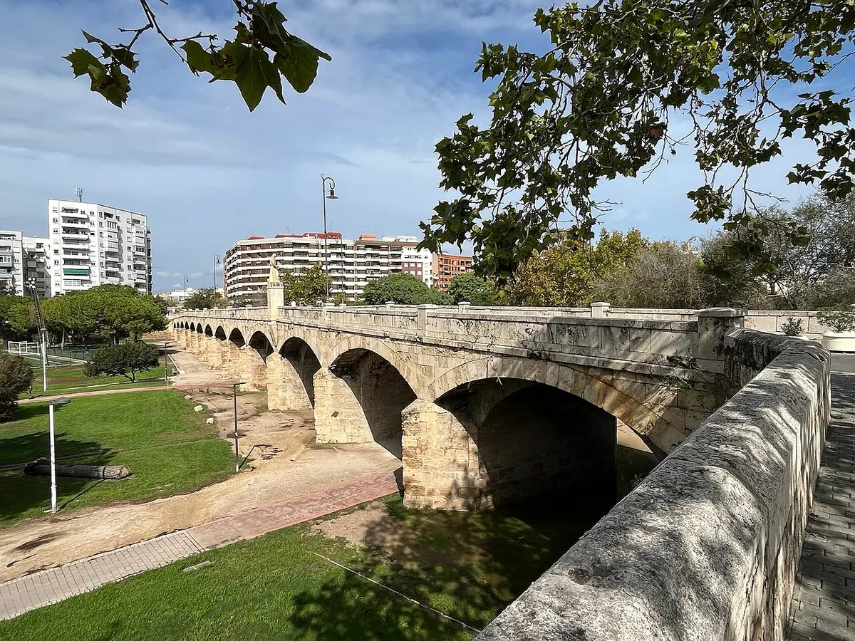 A stone bridge of several arches crossing the green, tree-lined bed of the old Turia river